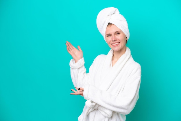 Jeune femme en peignoir isolé sur fond bleu tendant les mains sur le côté pour inviter à venir