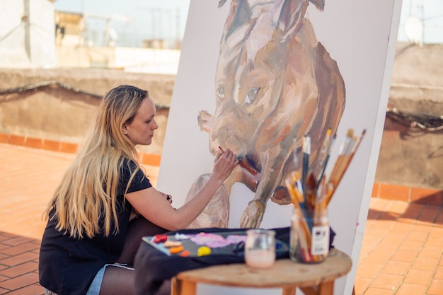 Jeune femme peintre dessinant sur le toit de la maison. Photo de bouledogue sur grande toile. Art en plein air