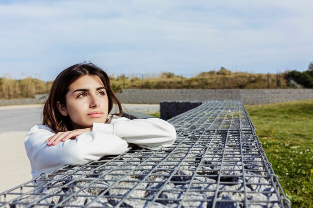 Photo jeune femme pensive et détendue assise sur un parc public tout en détournant les yeux