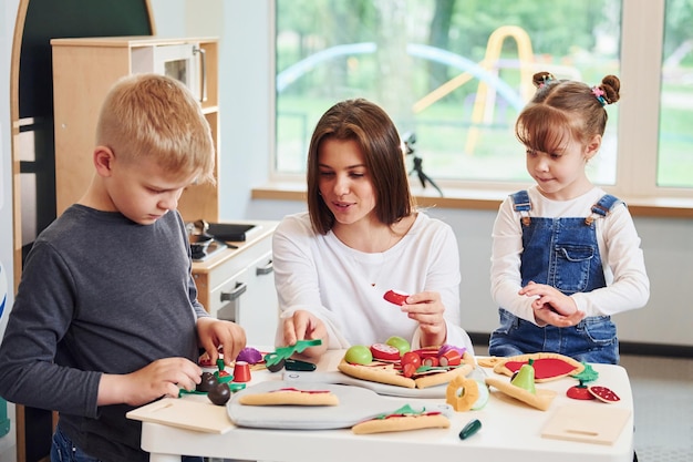 Jeune femme avec petit garçon et fille jouant avec des jouets ensemble dans la cuisine