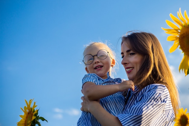 Jeune femme et une petite fille dans ses bras sur un champ de tournesol. Maman avec l'enfant.