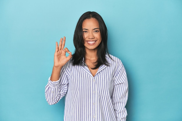 Une jeune femme philippine sur le studio bleu, joyeuse et confiante, montrant un bon geste.