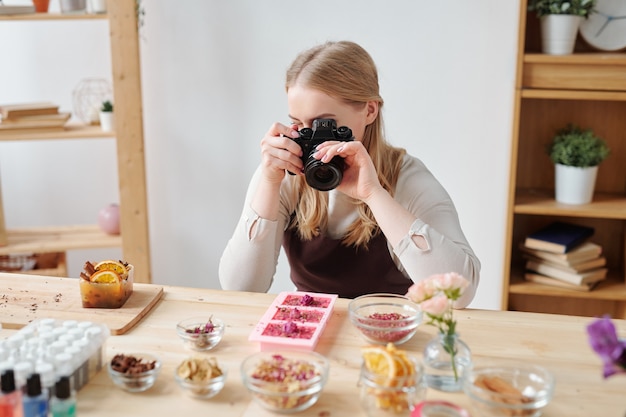 Jeune Femme Avec Photocamera Photographier Du Savon Artisanal Et Des Ingrédients Sur La Table En Studio