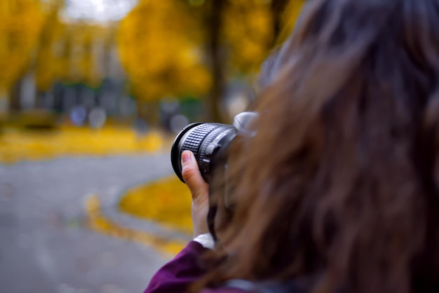 Jeune femme photographe avec un appareil photo prenant une photo dans le parc d'automne visage non montré