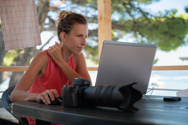 Jeune femme photographe éditant des photos sur son ordinateur portable pendant ses vacances dans une station balnéaire d'été.