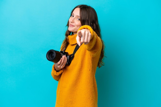 Jeune femme photographe isolée sur fond bleu pointe le doigt vers vous avec une expression confiante