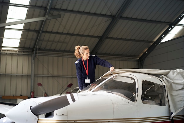 Jeune Femme Pilote Découvrant Des Avions Légers Avec Couvercle De Protection Dans Le Hangar