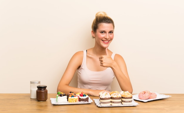 Jeune femme avec plein de mini gâteaux différents dans un tableau donnant un geste du pouce levé