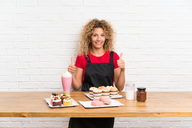 Jeune femme avec plein de mini gâteaux différents dans un tableau donnant un geste du pouce levé