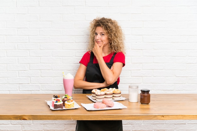 Jeune femme avec plein de mini gâteaux différents sur une table en pensant à une idée