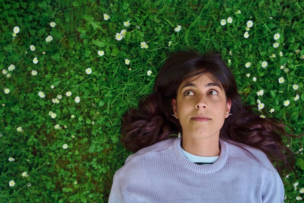 Jeune femme pleine d'espoir levant la pose sur l'herbe entourée de petites marguerites vue de dessus