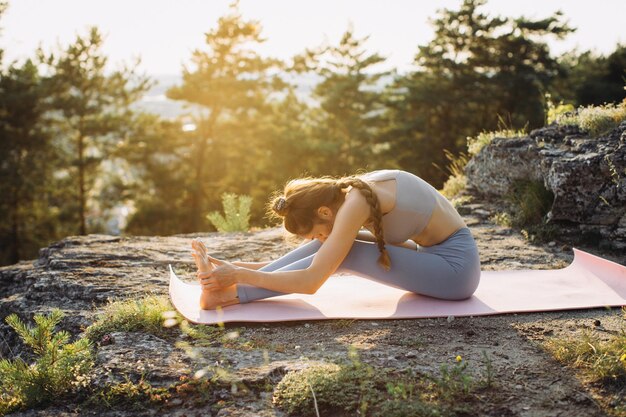 Une jeune femme en pleine forme pratique le yoga sur les rochers sur le fond de la forêt de pins.