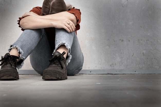 Jeune femme pleure et assise près d'un mur vide, solitaire, fille triste et déprimée, la tête baissée