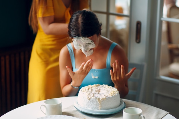 Jeune femme plonge le visage dans un gâteau blanc à la crème. Notion de joyeux anniversaire.