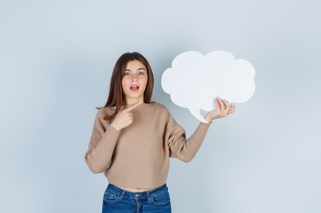 Jeune femme pointant sur papier bulle en pull, jeans et à la nostalgie, vue de face.