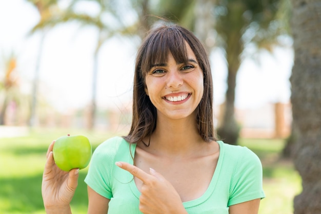 Jeune femme avec une pomme à l'extérieur et la pointant