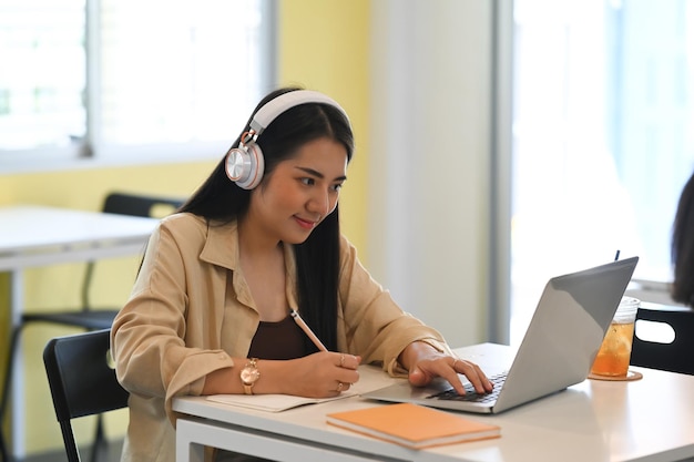 Jeune femme portant un casque d'apprentissage en ligne via un ordinateur portable assis au café.