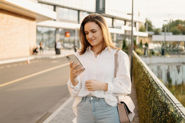 Jeune femme portant une chemise blanche regarde le téléphone et attend un taxi