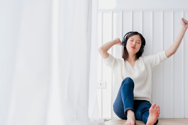 Une jeune femme portant des écouteurs alors qu'elle est assise sur le sol à la maison