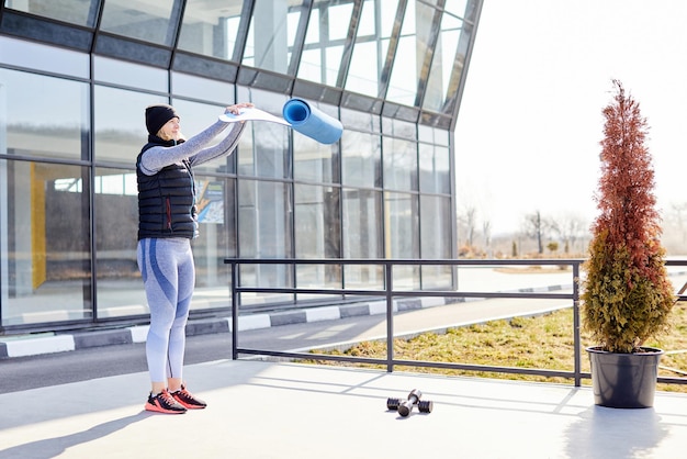 Une jeune femme portant un gilet noir et des vêtements de sport un tapis d'entraînement