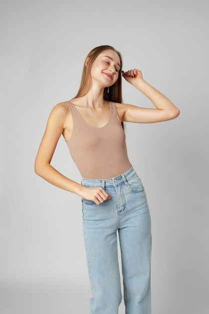 Une jeune femme portant des jeans de haute hauteur et un tank top posant sur un fond gris dans un studio