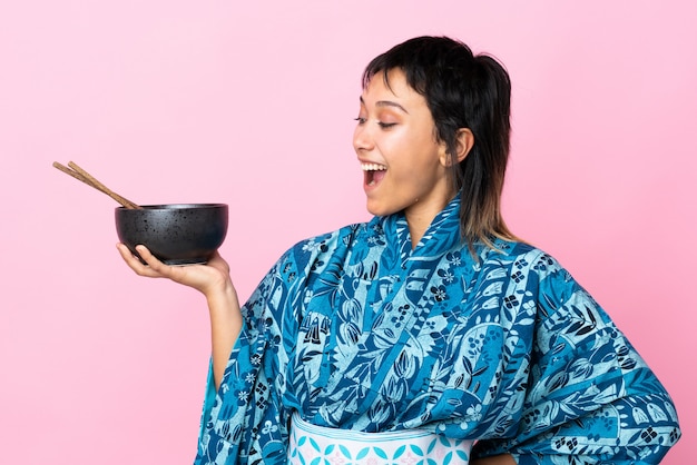 Jeune femme portant un kimono tenant un bol de nouilles sur un mur blanc isolé