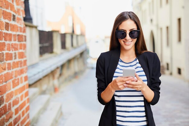 Jeune femme portant des lunettes de soleil à l'aide de téléphone à l'extérieur