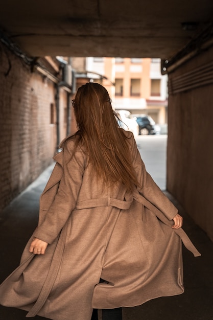 Jeune femme portant un manteau brun à la mode marchant dans les vieilles rues d'une ville