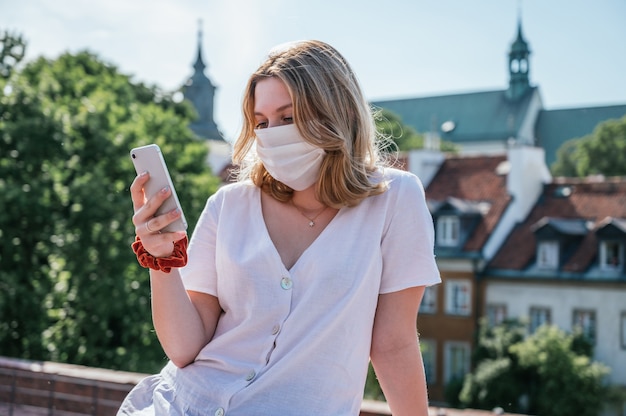 Jeune femme portant un masque facial et à l'aide de son smartphone