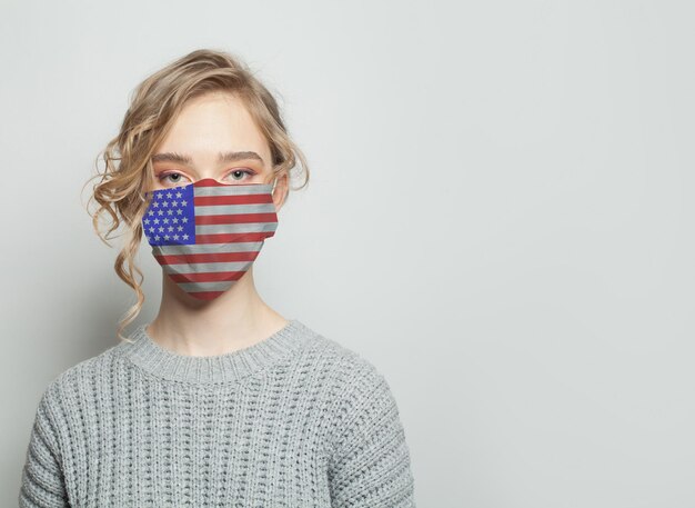 Une jeune femme portant un masque facial avec le drapeau national des États-Unis Concept d'épidémie de grippe et de protection contre le virus