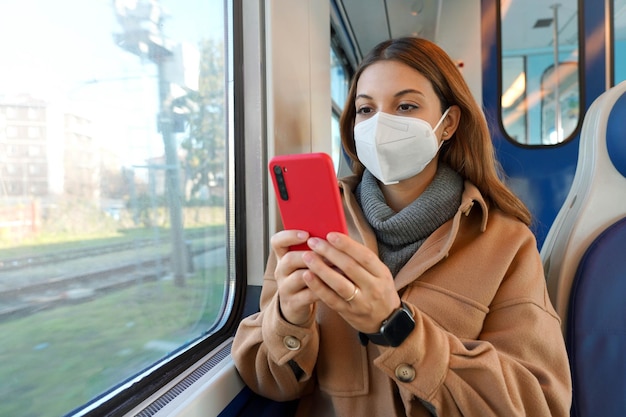 Jeune femme portant un masque facial FFP2 KN95 contre la lecture du coronavirus sur un smartphone voyageant dans les transports publics. Concept de soins de santé, de protection contre les virus et de voyage en toute sécurité.