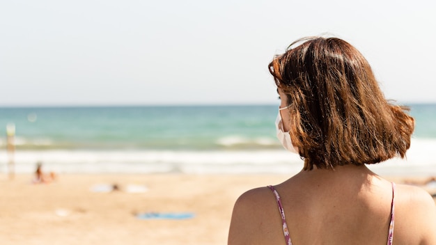 Jeune femme portant un masque facial sur la plage - Pandémie