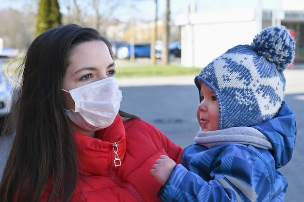 Une jeune femme portant un masque facial et tenant dans ses mains un petit garçon. Mesures protectives. Mère et enfant en quarantaine.