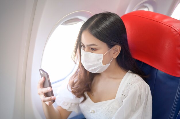 Une jeune femme portant un masque facial utilise un smartphone à bord, un nouveau voyage normal après le concept de pandémie de covid-19