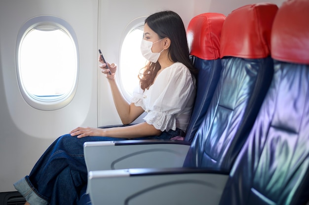 Une jeune femme portant un masque facial utilise un smartphone à bord, un nouveau voyage normal après le concept de pandémie de covid-19