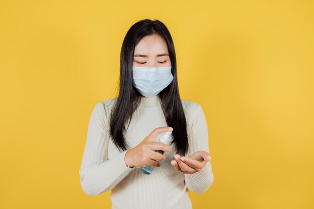 Jeune femme portant un masque médical En appuyant sur le gel d'alcool sur fond jaune, masque médical pour protéger Covid-19 (Coronavirus)