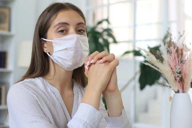 Jeune femme portant un masque médical à la maison en situation épidémique.