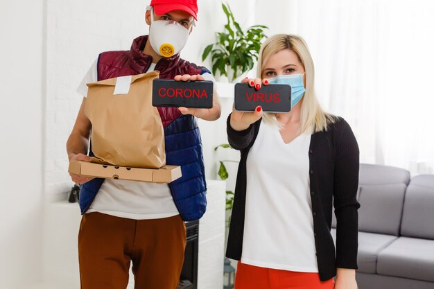 Jeune femme portant un masque médical recevant un colis du livreur à l'intérieur. Prévention de la propagation du virus