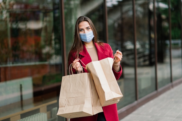 Jeune femme portant un masque pour prévenir le virus avec des sacs à provisions sur une rue étroite en Europe.