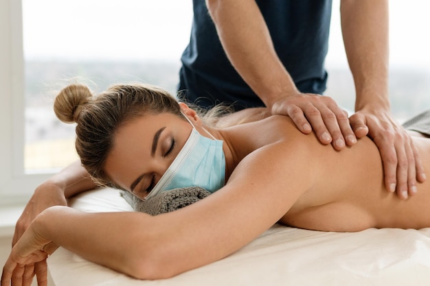 Jeune femme portant un masque de prévention pendant la séance de massage du dos