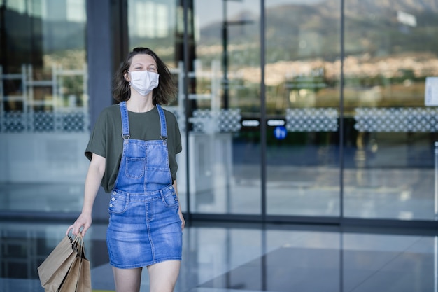 Une jeune femme portant un masque de protection contre le coronavirus quitte le centre commercial heureux après avoir effectué ses premiers achats après la qurentena par Covid.