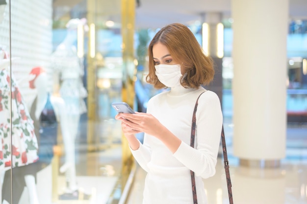 Une jeune femme portant un masque de protection dans un centre commercial, faisant du shopping sous le concept de pandémie de Covid-19.