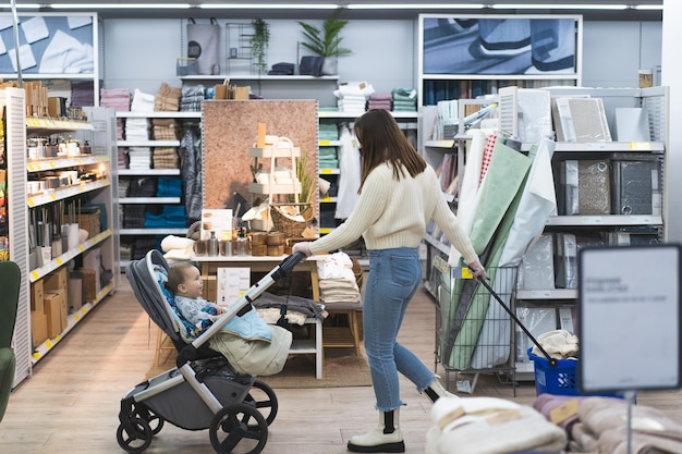 Jeune femme portant un masque de protection et des gants de protection en magasin avec un bébé dans une poussette