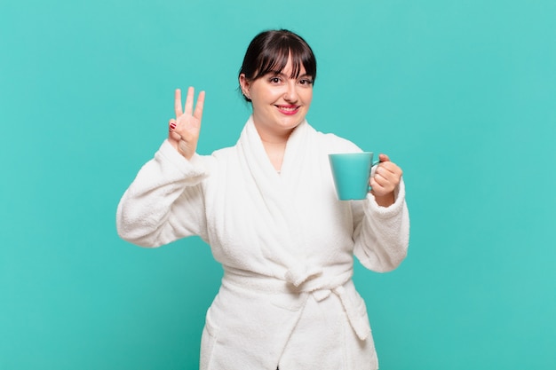 Jeune femme portant un peignoir souriant et à l'air sympathique, montrant le numéro trois ou troisième avec la main vers l'avant, compte à rebours