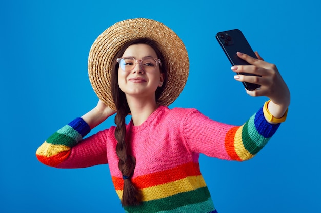 Jeune femme portant un pull arc-en-ciel et des lunettes prenant un selfie avec un smartphone