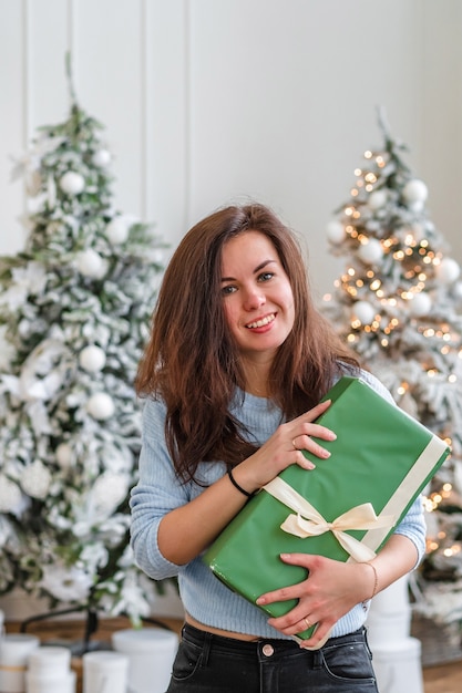 Jeune femme portant un pull douillet, ouvrant un cadeau à l'arbre de Noël à la maison