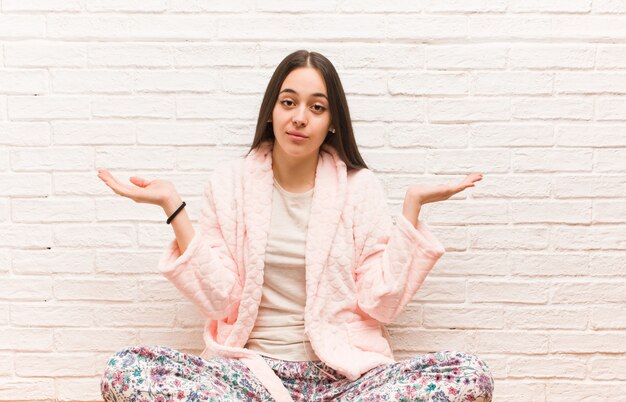 Jeune femme portant un pyjama doutant et haussant les épaules