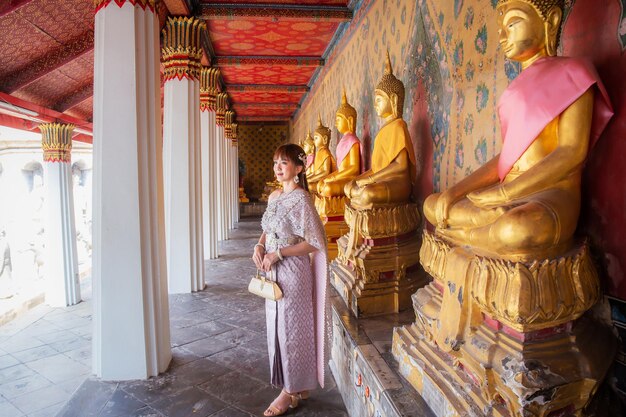 Photo une jeune femme portant une robe thaïlandaise avec des accessoires portant un sac à wat arun ratchawararam où de nombreuses statues de bouddha sont rangées c'est une destination populaire pour les touristes du monde entier bangkok thaïlande