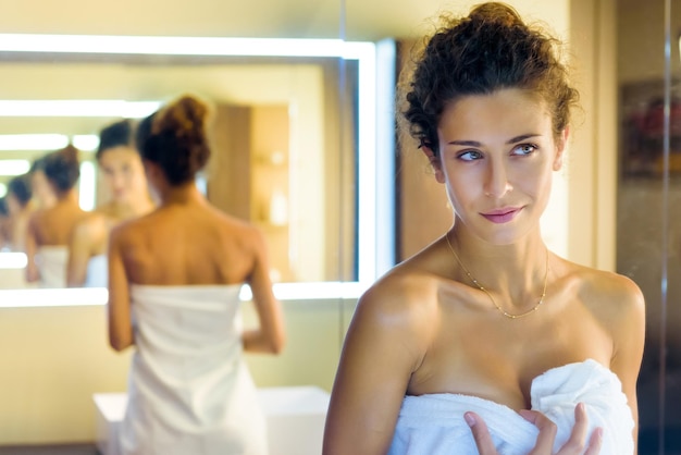 Une jeune femme portant une serviette debout dans la salle de bain