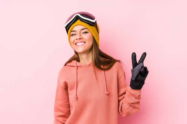 Jeune femme portant un vêtement de ski montrant le signe de la victoire et souriant largement